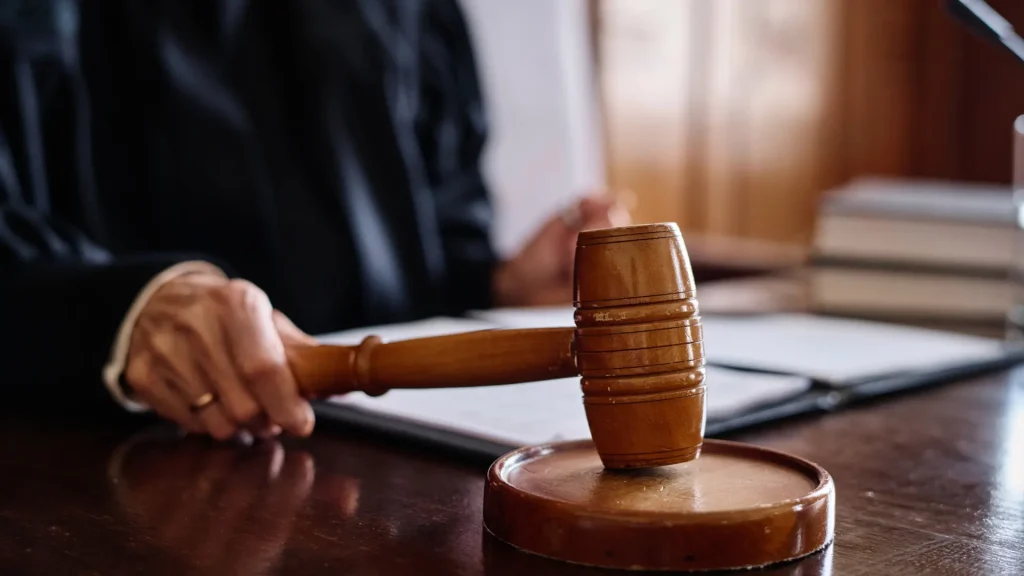 A wooden gavel resting on a judge's desk, with a blurred background of legal documents.